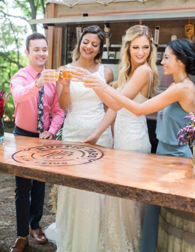 Brides and guest cheering their beers infront of rustic tap truck